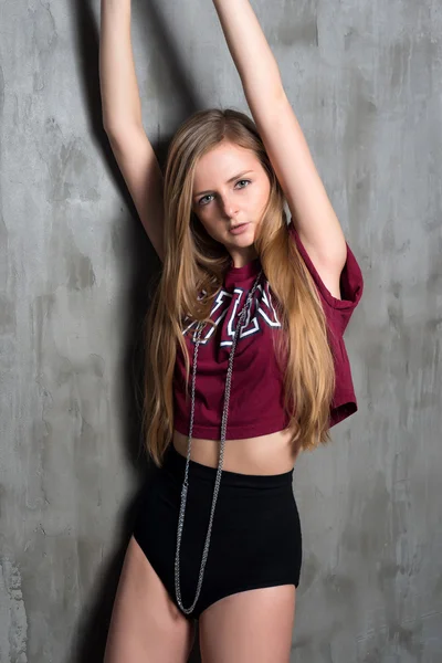 Sexy young blonde woman in black luxury lingerie and sports t-shirt posing against grungy gray wall. Passion and desire pose. Attractive woman with long precious chain. — Stock Photo, Image