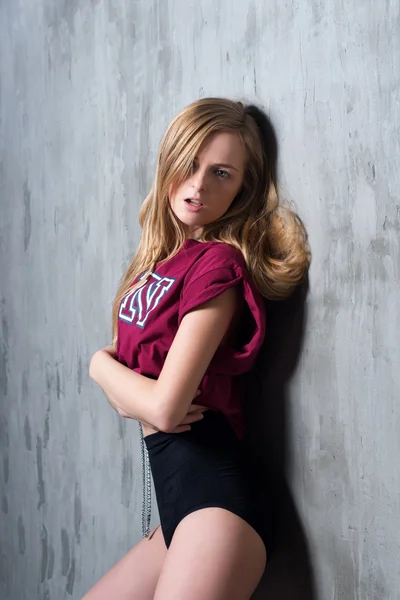 Sexy mujer rubia joven en lencería de lujo negro y camiseta deportiva posando contra la pared gris grumosa. Pasión y deseo posan. Mujer atractiva con cadena larga y preciosa . — Foto de Stock