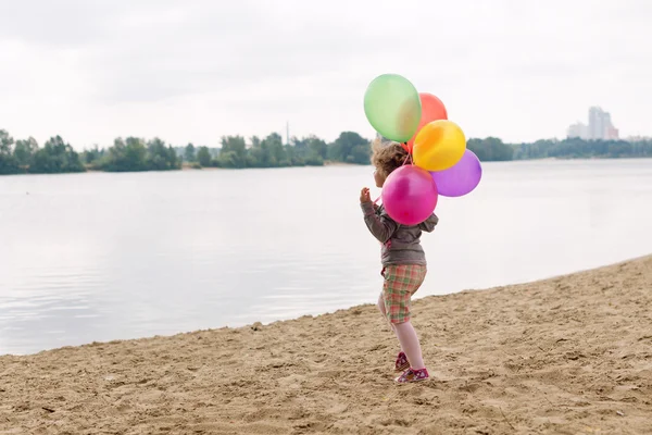 Petite fille avec des ballons sur la rive sablonneuse de la rivière ou du lac . — Photo