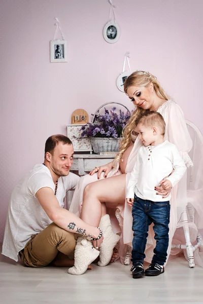 Uma família feliz com uma criança na sala de estar rosa abraçando uns aos outros . — Fotografia de Stock