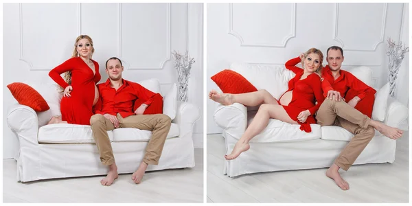 Onnellinen nuori raskaana oleva pari pukeutunut punaiseen syleillä toisiaan sohvalla valkoisessa olohuoneessa — kuvapankkivalokuva