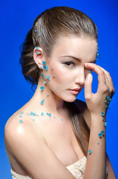 Piękna młoda kobieta nago pokryta niebieskie kryształy na niebieskim tle. — Zdjęcie stockowe