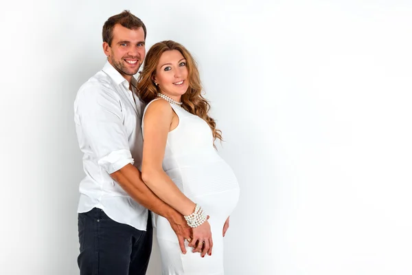 Happy Pregnant Couple dressed in white embrace each other on a white background — Stock Photo, Image