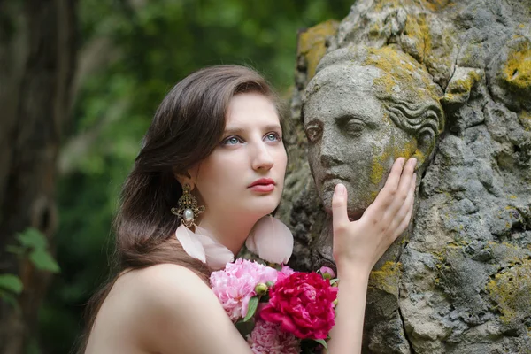 Krásná mladá nahá žena s antické sochy a kytici květin. Srovnání živé ženské krásy a umění starověkého sochařů. — Stock fotografie