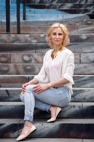 Moda de verano al aire libre impresionante retrato en bastante joven rubia sexy mujer vestida con una camisa blanca y pantalones vaqueros rasgados divertirse en la calle — Foto de Stock