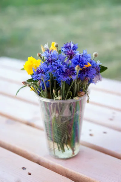 Boeket van wilde bloemen in kunststofglas op houten tafel. — Stockfoto