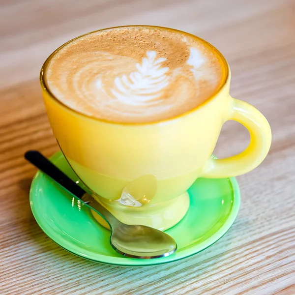 Una taza de café con leche en una taza amarilla brillante sobre fondo de madera — Foto de Stock