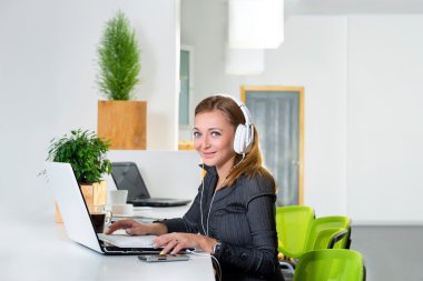 Kulaklık dizüstü bilgisayar modern parlak ofis, internet'te sörf ile genç başarılı işkadını. Tablet bilgisayar kullanarak ve kahve molası sırasında müzik kadın.