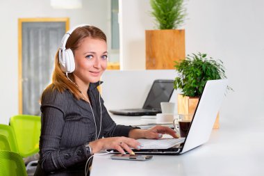 Kulaklık dizüstü bilgisayar modern parlak ofis, internet'te sörf ile genç başarılı işkadını. Tablet bilgisayar kullanarak ve kahve molası sırasında müzik kadın.