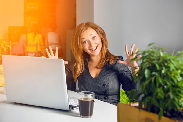 Opgewonden gelukkig zakenvrouw met opgeheven armen zitten aan de tafel met laptop vieren van haar succes. Grappig beeld van winnaar of verrast kantoor werknemer. Groene eco office concept. — Stockfoto