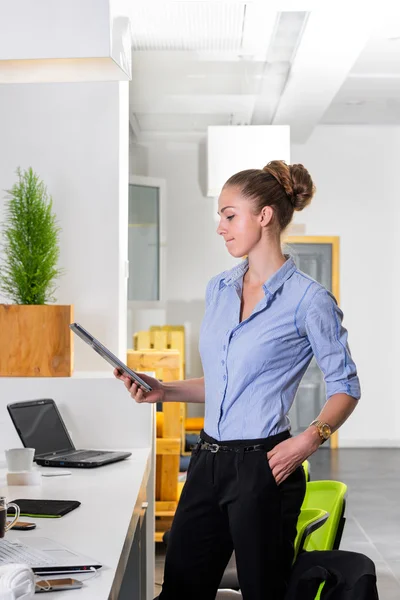 Jonge zakenvrouw in modern helder kantoor die de tablet met een lijst van taken. Bedrijfsconcept van kantoorwerk. — Stockfoto