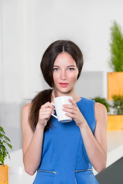 Jonge zakenvrouw holding een kop van koffie. Mooi meisje koffie of thee drinken in café. Mooie jonge vrouw met de kop warme drank camera kijken. — Stockfoto