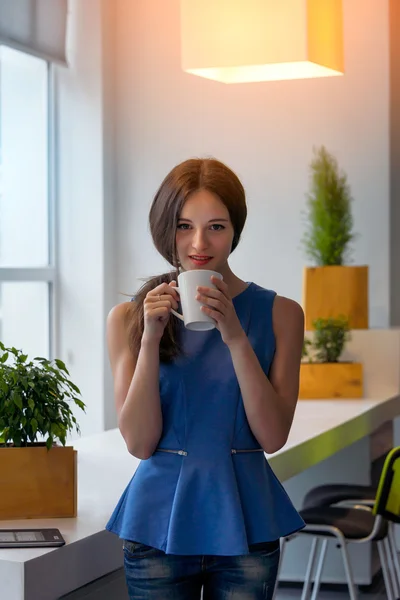 Jonge zakenvrouw holding een kop van koffie. Mooi meisje koffie of thee drinken in café. Mooie jonge vrouw met de kop warme drank camera kijken. — Stockfoto