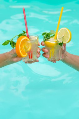 Mavi bir havuz üzerinde meyve ve nane ile süslenmiş renkli kokteyller. Rahatlık, yaz tatili ve tropikal tatil atmosferlerini tasvir etmek için mükemmel..