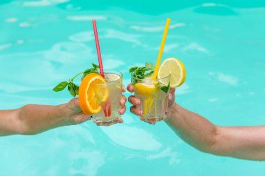 Mavi bir havuz üzerinde meyve ve nane ile süslenmiş renkli kokteyller. Rahatlık, yaz tatili ve tropikal tatil atmosferlerini tasvir etmek için mükemmel..