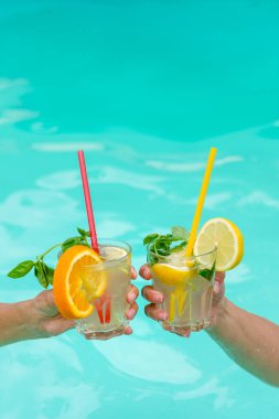 Mavi bir havuz üzerinde meyve ve nane ile süslenmiş renkli kokteyller. Rahatlık, yaz tatili ve tropikal tatil atmosferlerini tasvir etmek için mükemmel..