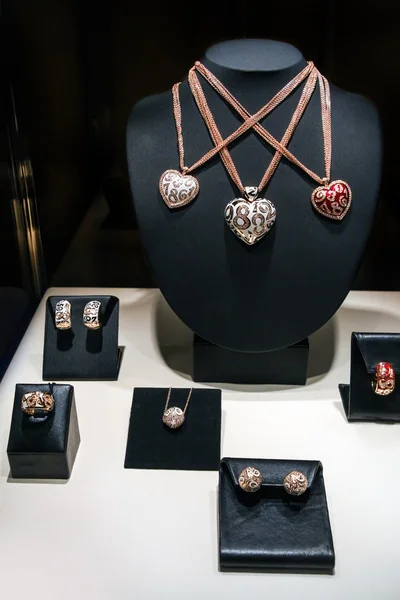 Tre collane in oro bianco e rosa su uno stand. Ciondoli a forma di cuore con diamanti. Set di gioielli di lusso con anelli e orecchini. Accessori donna di lusso sugli stand . — Foto Stock