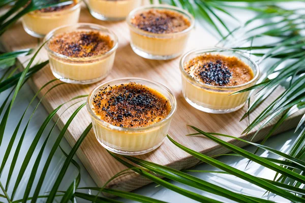 Creme brulee ahşap tepsi üzerinde palmiye yaprakları ile süslenmiş. Geleneksel Fransız vanilya krem tatlı üstüne caramelised şeker.