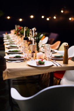 Süslü Noel tatili masası akşam yemeği için hazır. Restorandaki etkinlik için mumlar, ladin dalları, tabaklar ve peçetelerle süslenmiş güzel bir masa takımı..