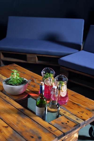 Uma garrafa de bebida frutada com hortelã e limão e duas garrafas de vinho em uma mesa de paletes pronta para o jantar . — Fotografia de Stock