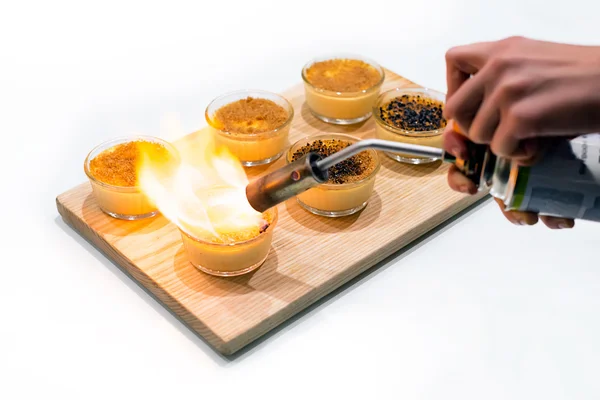 Womans hands making creme brulee with gas-burner on wooden tray. Traditional French vanilla cream dessert with caramelised sugar on top. — Stock Photo, Image