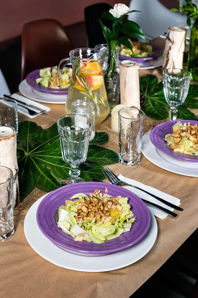 Fresh salad with chicken meat, oranges, walnuts, greens and herbs and olive oil on a decorated table ready for dinner. Beautifully decorated table set for wedding or another event in the restaurant.
