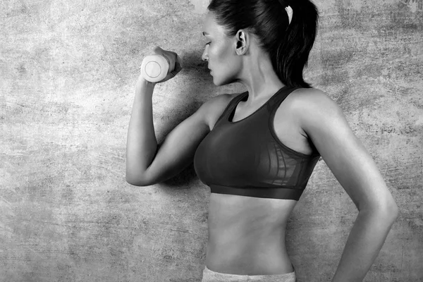 Mujer en forma de ejercicio con pesas en el fondo de una pared de hormigón en el gimnasio. concepto de estilo de vida saludable . — Foto de Stock