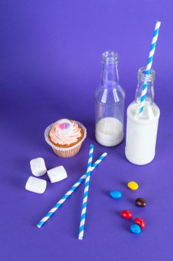 Cupcake for Valentine's Day with hearts on top of whipped cream and milk cocktails with retro cocktail tubes, served in bottles on colourful background.