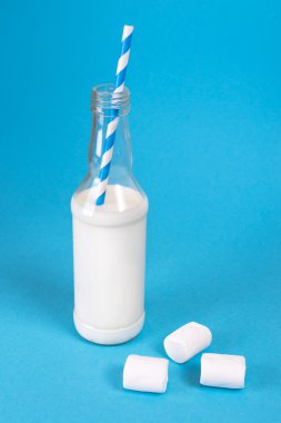 Milk cocktail with retro cocktail tube, served in bottle on colorful background with sweet marshmallows.