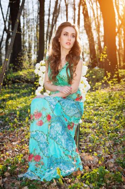 Güzel genç kadın yaz bahçesinde gülile bir sandalyede oturuyor. Güzellik yaz.