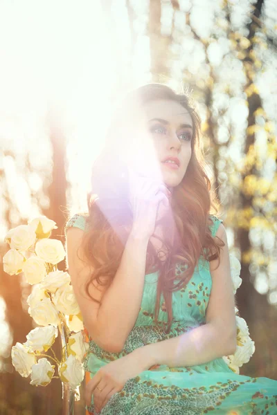 Beautiful young woman in summer garden sitting on a chair with roses. Beauty summertime. — Stock Photo, Image