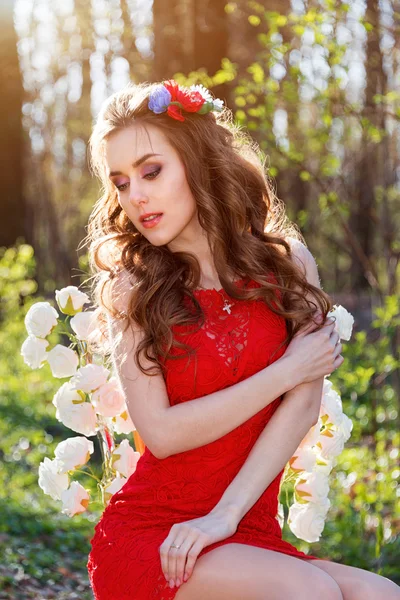 Vacker ung kvinna i sommarträdgård sitter på en stol med rosor. Skönhet sommartid. — Stockfoto