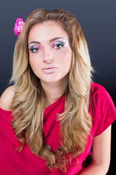 Beautiful blonde girl with bright makeup and long curled hair  on gray background. Fashion shot. — Stock fotografie