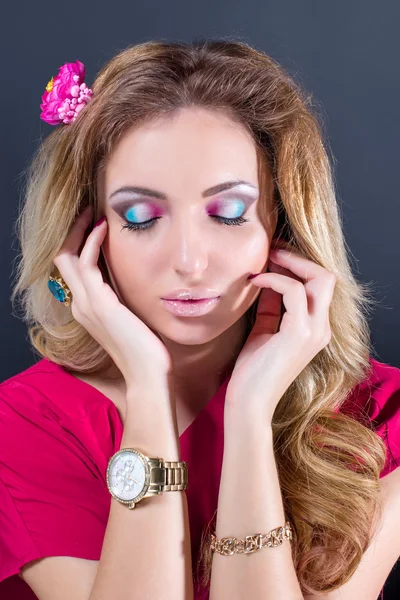 Beautiful blonde girl with bright makeup, long curled hair and massive jewelry on grey background. Fashion shot. — Stock fotografie