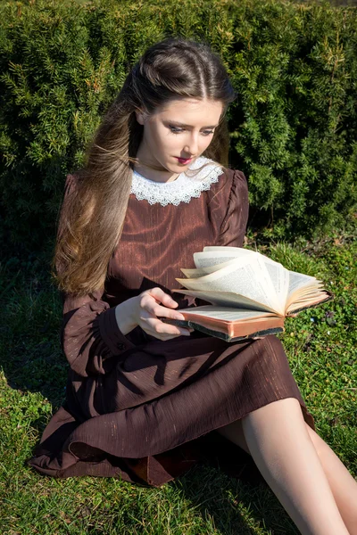 Romantische jonge vrouw die een boek leest in de tuin zittend op het gras. Ontspan buiten tijd concept. — Stockfoto