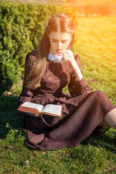 Bahçede kitap okuyan romantik genç bir kadın çimlerin üzerinde oturuyor. Açık hava zaman kavramını gevşetin. — Stok fotoğraf