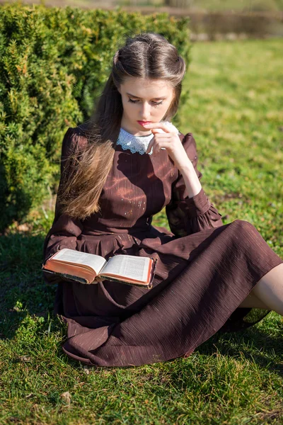 Bahçede kitap okuyan romantik genç bir kadın çimlerin üzerinde oturuyor. Açık hava zaman kavramını gevşetin. — Stok fotoğraf