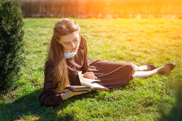 Bahçede kitap okuyan romantik genç bir kadın çimlerin üzerinde oturuyor. Açık hava zaman kavramını gevşetin. — Stok fotoğraf