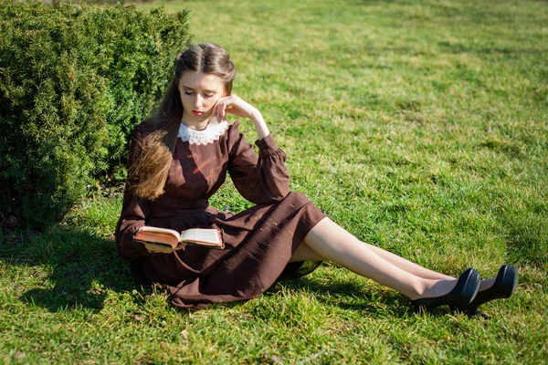 Mujer joven y romántica leyendo un libro en el jardín sentado en la hierba. Relajarse concepto de tiempo al aire libre. — Foto de Stock