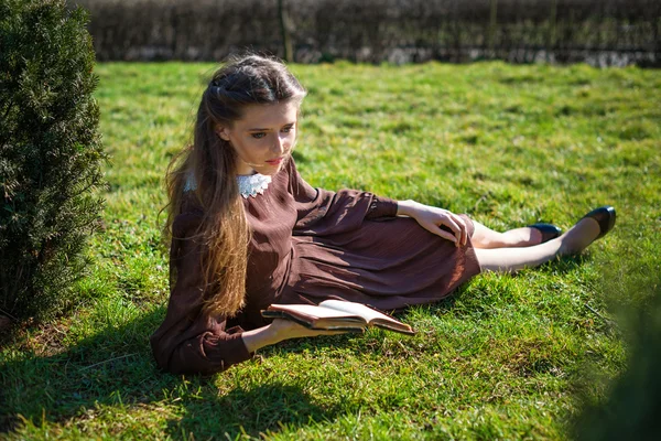 Mujer joven y romántica leyendo un libro en el jardín sentado en la hierba. Relajarse concepto de tiempo al aire libre. —  Fotos de Stock