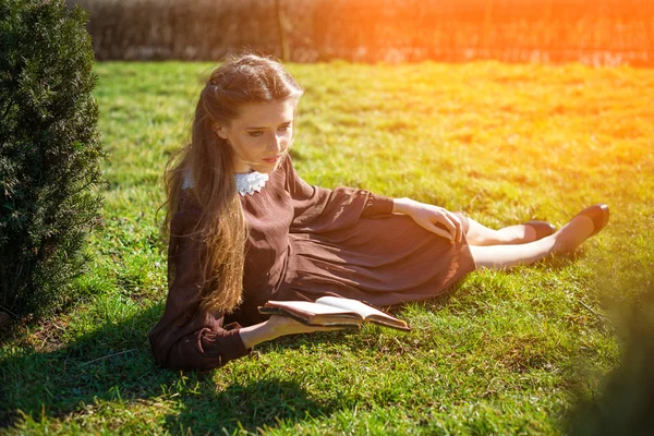 Ρομαντικό νεαρή γυναίκα διαβάζει ένα βιβλίο στον κήπο κάθεται στο γρασίδι. Χαλαρώστε έννοια εξωτερική ώρα. — Φωτογραφία Αρχείου