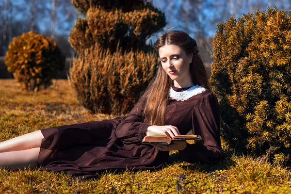 Romantische junge Frau beim Lesen eines Buches im Garten auf dem Rasen sitzend. Entspanntes Outdoor-Zeitkonzept. — Stockfoto