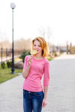 Redhead beautiful young woman biting a lollipop. Pretty girl having fun outdoors.