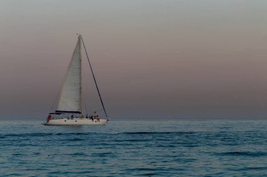 Deniz ufkunda pembe gökyüzünün arka planına karşı bir yat.