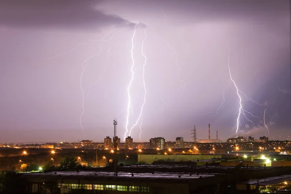 Powerful lightning strike hits the city at night. A strong lightning strike over a dark gray sky hits the ground, illuminating the town