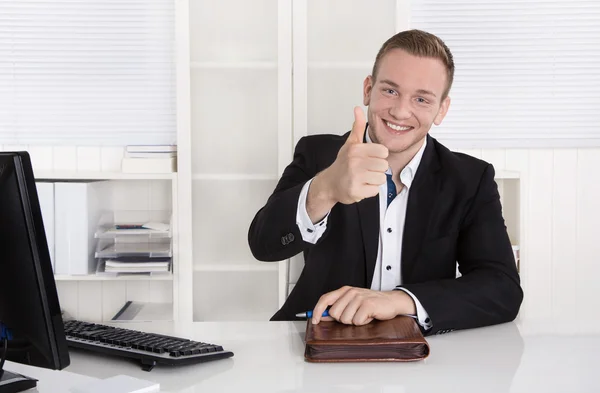 Glücklicher junger Geschäftsmann sitzt in seinem Büro und hebt den Daumen — Stockfoto