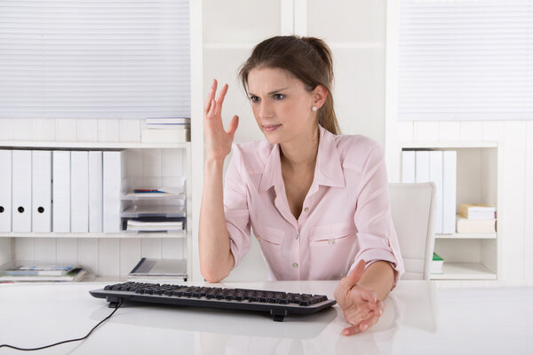 Злая и шокированная молодая женщина, сидящая в офисе в розовом
