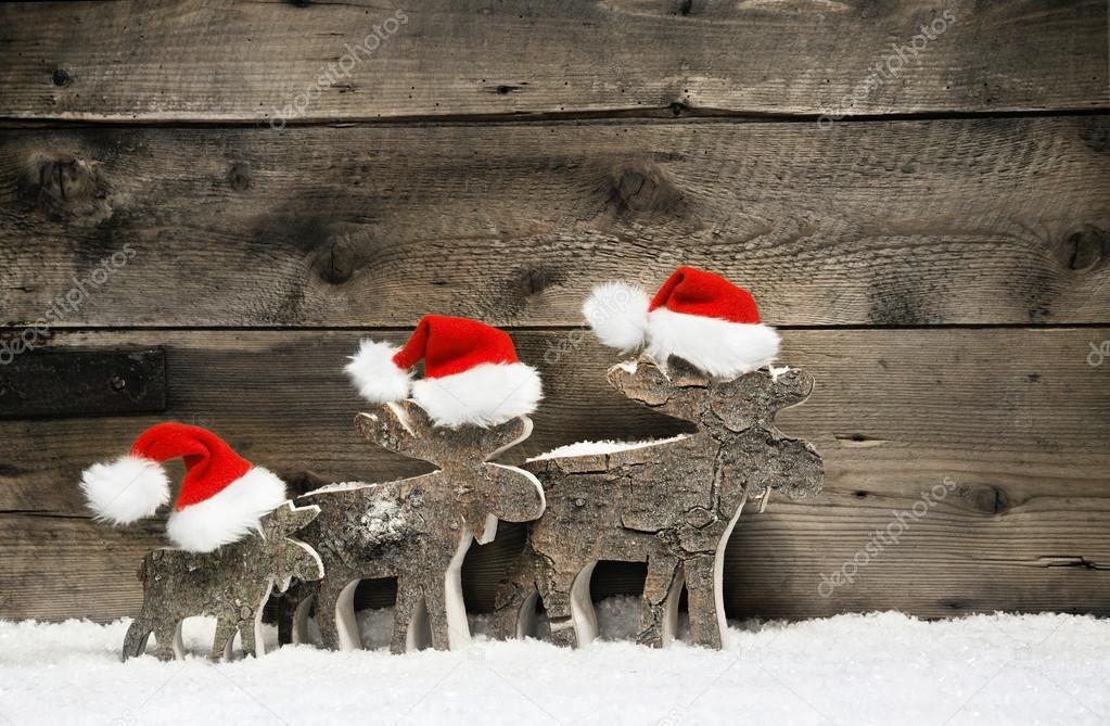 Three reindeer wearing santa hats on brown wooden background.