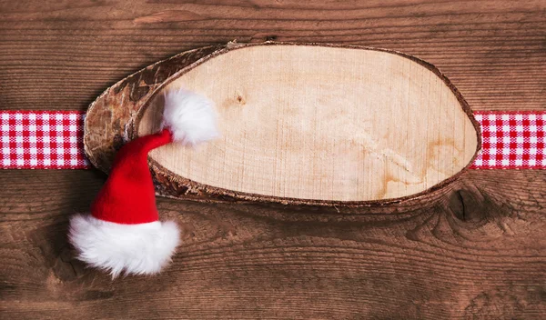 Rusztikus, fából készült karácsonyi kártya vagy hirdetőtábla, santa kalap és piros — Stock Fotó