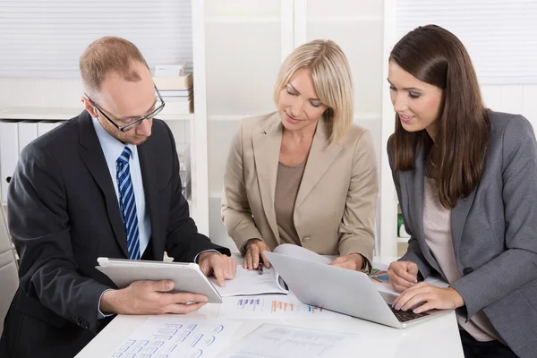 Team av tre affärsmän sitter tillsammans vid skrivbord i ett möte — Stockfoto